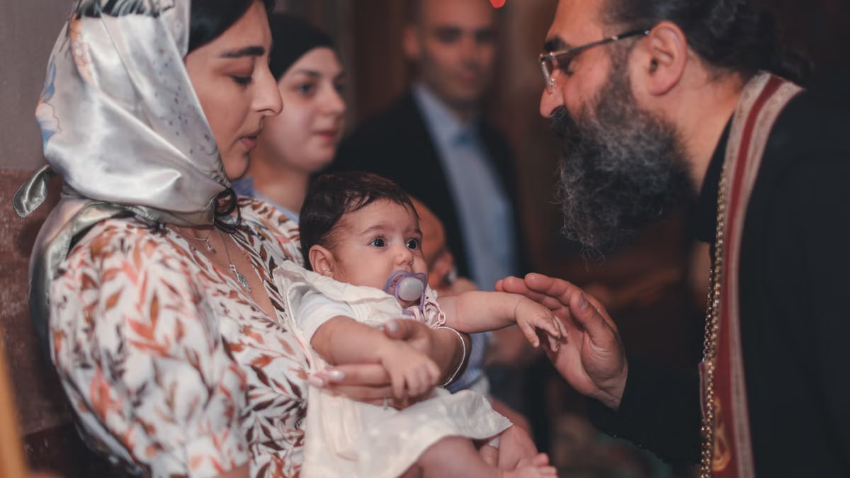 A touching moment during a baby's baptism ceremony, featuring a priest and family.